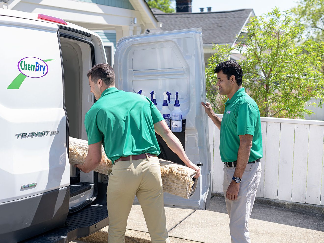Two Chem-Dry technicians loading a rolled rug into a Chem-Dry van